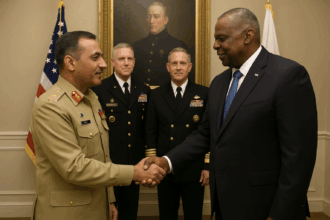 General Asim Munir, wearing a Pakistan Army uniform, shakes hands with US Secretary of Defense Lloyd Austin, dressed in a dark suit and blue tie. Two US military officers stand in the background with American flags behind them, creating a formal diplomatic setting.