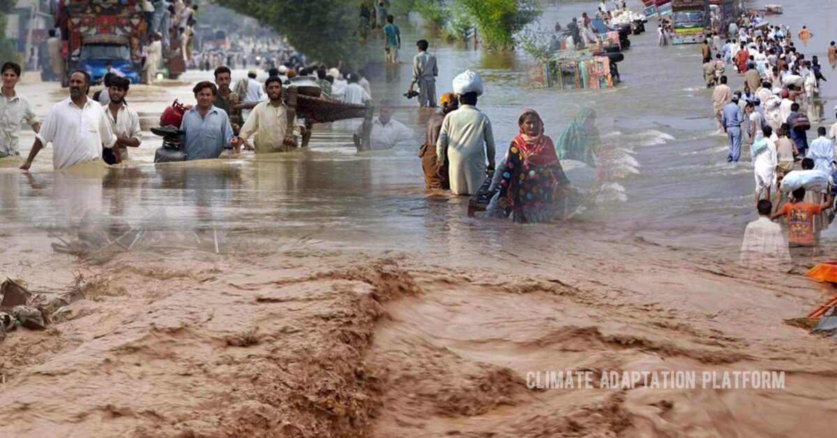 People wading through floodwaters in Pakistan as heavy monsoon rains cause severe flooding, destroying homes, displacing families, and blocking roads.