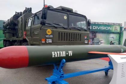 Pakistan’s Fatah-IV cruise missile displayed on a blue stand in front of a military truck at a defense exhibition.
