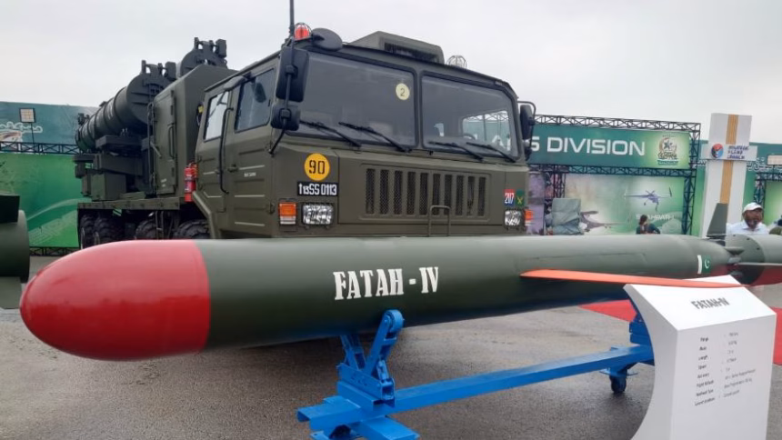 Pakistan’s Fatah-IV cruise missile displayed on a blue stand in front of a military truck at a defense exhibition.