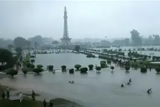 Flooded streets and heavy rain in Punjab, Pakistan during the 10th spell of monsoon rains, with people navigating through rainwater and dark stormy clouds overhead.