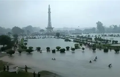 Flooded streets and heavy rain in Punjab, Pakistan during the 10th spell of monsoon rains, with people navigating through rainwater and dark stormy clouds overhead.
