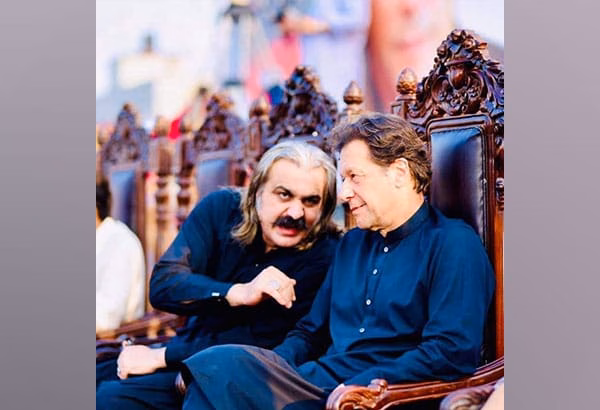 Imran Khan and Ali Amin Gandapur in traditional black attire sitting on ornate chairs, engaged in a serious conversation during a public event.