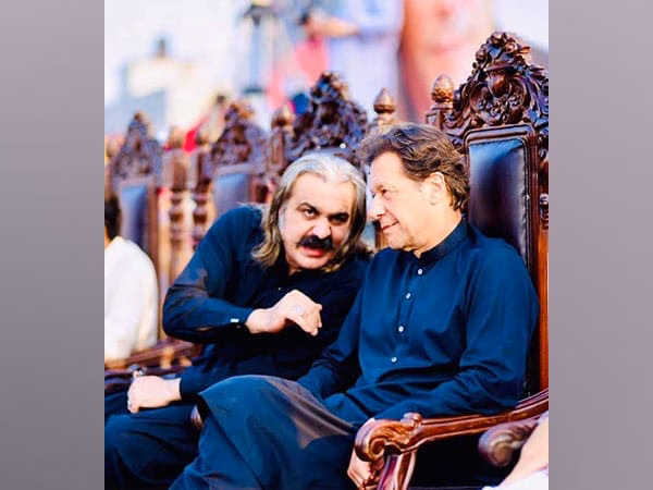 Imran Khan and Ali Amin Gandapur in traditional black attire sitting on ornate chairs, engaged in a serious conversation during a public event.